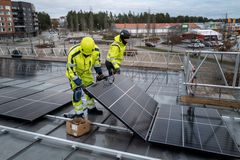 Två byggnadsarbetare arbetar med installation av solcellsanläggning på taket av en skola.
