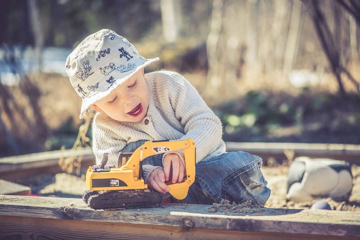 En liten pojke med hatt leker med en gul grävmaskin i en sandlåda.