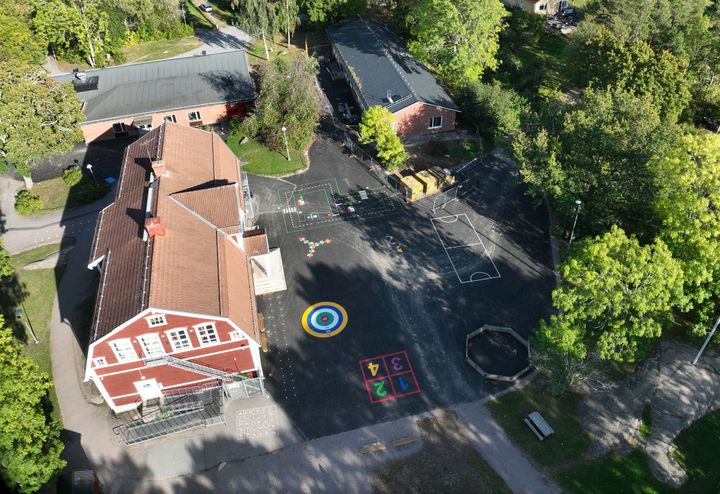 Bälinge skolas nyrenoverade skolgård med asfaltsmålningar och grönytor, sedd ur helikopterperspektiv.