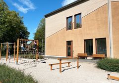 Skolgård med klätterställning och lekytor nära en gul byggnad.