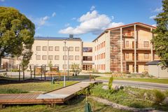 Två moderna skolbyggnader i soligt väder, omgivna av träd och grönområden.