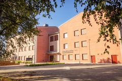 En modern röd tegelbyggnad med flera våningar, omgiven av träd och grönska.