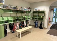 En skolentré med gröna fack, klädhängare och plastlådor.