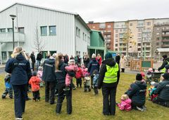 En grupp barn och vuxna står utomhus vid en förskola.