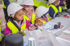 Barn i skyddshjälmar och reflexvästar sitter vid ett bord utomhus och äter bakverk.