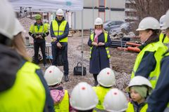 Byggarbetsplats med vuxna och barn i hjälmar och reflexvästar, några står och några sitter på huk.