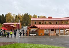 Nybyggd förskola i rött tegel med människor samlade utanför, omgiven av höstskog.