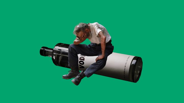 En man sitter med huvudet i handen på en stor flaska mot grön bakgrund.