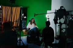 En person sitter i en studio med filmutrustning och en grön skärm i bakgrunden.