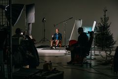 Person sitter i en inspelningsstudio omgiven av ljusutrustning och en kameraman medan inspelning pågår.