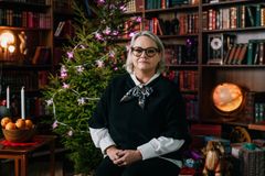 Kvinna sitter i ett rum med en julgran och bokhyllor i bakgrunden.