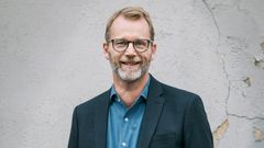 Joakim Ramsberg i kostym och glasögon står framför en ljus vägg.