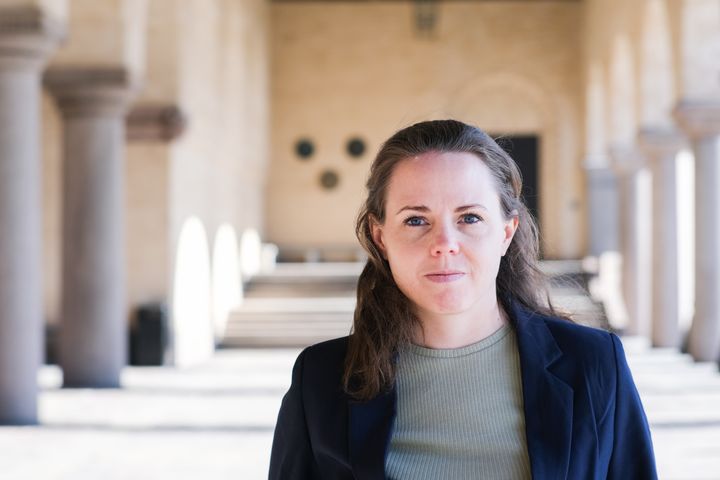 Alexandra Mattsson står i en mörk kavaj med stadshusets kolonner och valvbågar i bakgrunden.