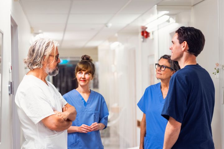 Fyra personer, två män och två kvinnor yrkesverksamma inom vården, står i en korridor och pratar.