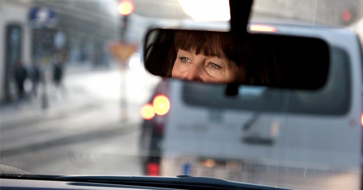 En person som kör bil och som tittar i backspegeln.