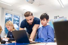 Skolmiljö där pedagog visar något för en elev på datorn.