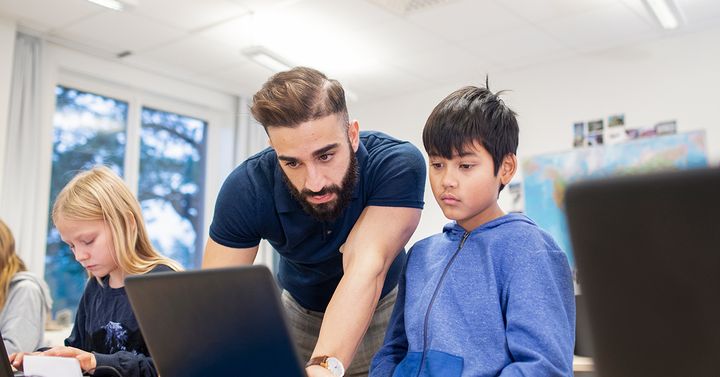 Skolmiljö där pedagog visar något för en elev på datorn.