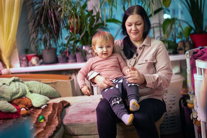 Kvinna med ett litet barn i knät sitter inomhus, omgivna av växter.