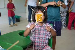 En ung flicka visar stolt upp sin konstverk i ett klassrum. Hon och andra barn deltar i en aktivitet där de skapar med garn och pinnar.