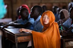 Elev iklädd orange sjal sitter vid en skolbänk i ett klassrum.