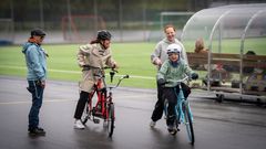En grupp personer hjälper varandra att cykla på en inhägnad bana.