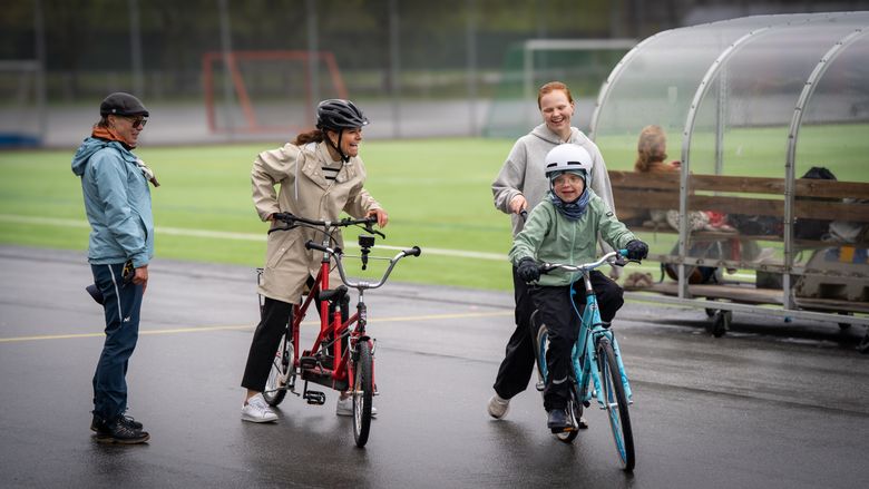 En grupp personer hjälper varandra att cykla på en inhägnad bana.