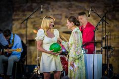 Alt-text: En person i ljus klänning tar emot en utmärkelse av en annan person i blommig klänning vid en konsert.