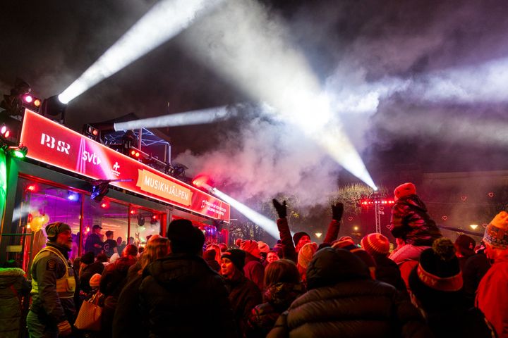 Mängd människor framför en upplyst scen under Musikhjälpens evenemang på kvällen.