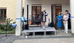 En kvinna på scen och flera andra människor som står vid sidan om och ler.