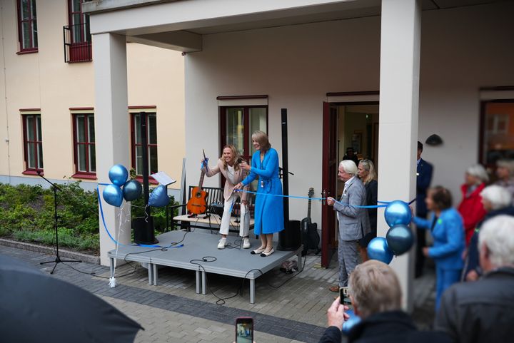 Två kvinnor vid ett blått invigningsband. De ler. En av dem står med en guldig sax.