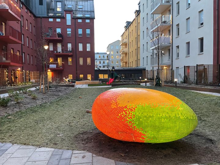 En stor mango i glasmosaik på en innergård, omringad av lägenhetshus