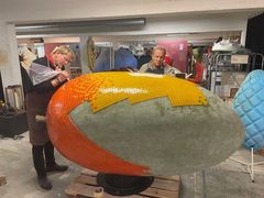 Två män fäster glasmosaikbitar på en stor mangostaty