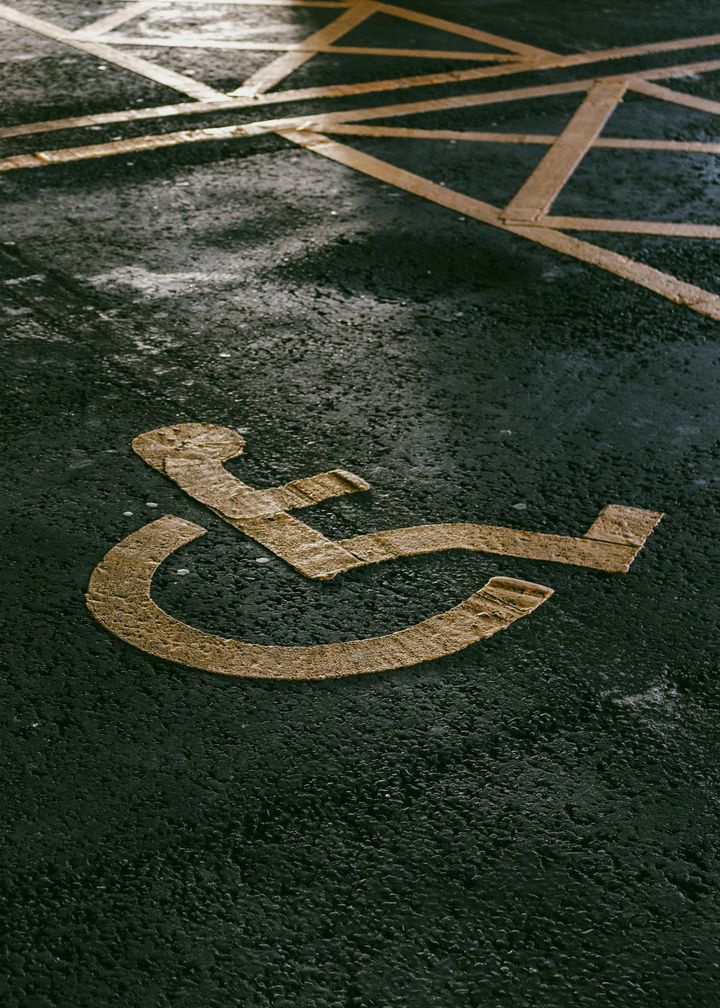 En rullstolssymbol syns på asfalten på en mörk parkeringsplats.