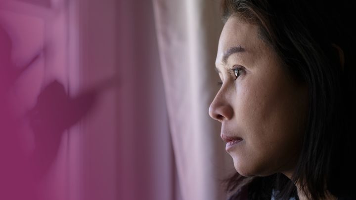 Kvinna, fotograferad i profil, tittar ut genom ett fördraget fönster. Kvinnan har en dämpad uppsyn. (Fotografi).