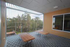 Alt text: Utrymme med träbänkar och rutigt golv i rättspsykiatrisk enhet, utsikt över träd.