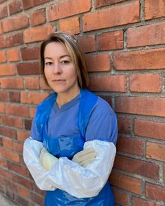 Person i blå skyddsdräkt står lutad mot en tegelvägg.