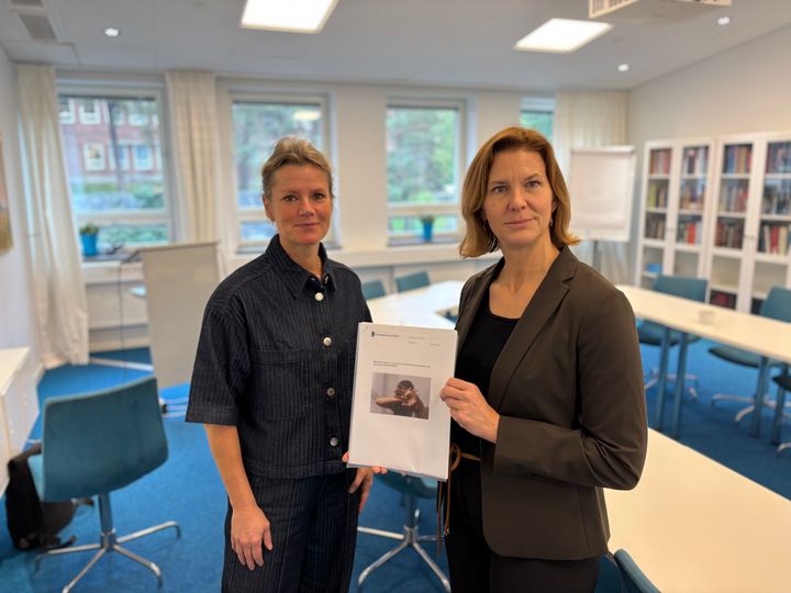Två personer står i ett konferensrum, en av dem håller i en rapport.