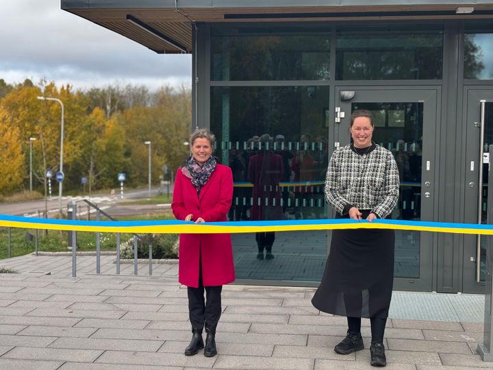 Två kvinnor klipper blågult band utanför en byggnad.