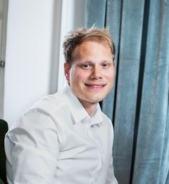 En man i vit skjorta sitter vid ett fönster.