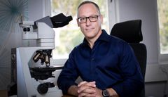 Person sittande vid ett mikroskop i ett kontor med fönster i bakgrunden.