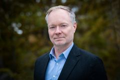 Man i kostym framför en suddig bakgrund av träd.