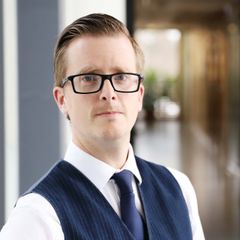 En glasögonprydd man med väst och slips står i en korridor