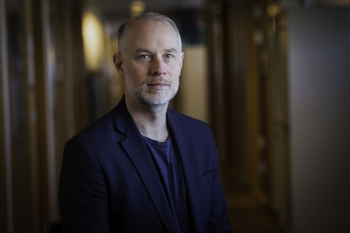 En person sitter i en korridor och bär en mörk kavaj.