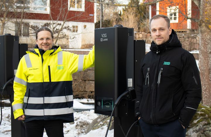Två män står vid en svart laddstation för elbilar.