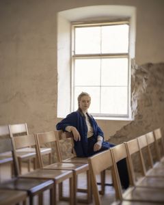 En kvinna sitter ensam på en stol bland andra tomma stolar.