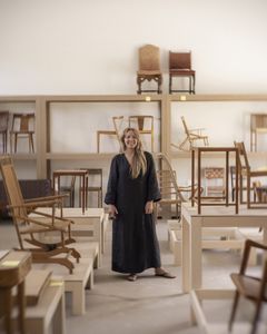 En kvinna står inomhus bland många stolar i en utställningsmiljö.