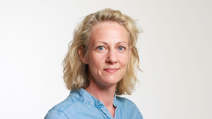 Kvinna med lust hår tittar in i kameran och ler.
