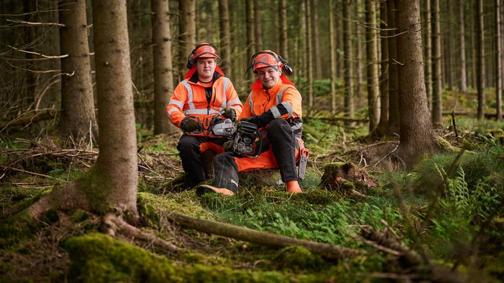 Två personer med arbetskläder som sitter på huk i skogen