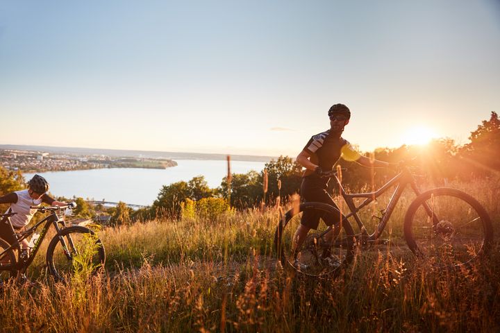 Cyklister på väg upp för backe i solnedgång med en sjö i bakgrunden