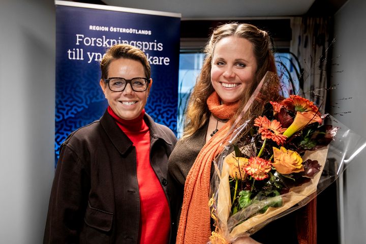 Två leende kvinnor, den ena håller en blombukett i famnen.
